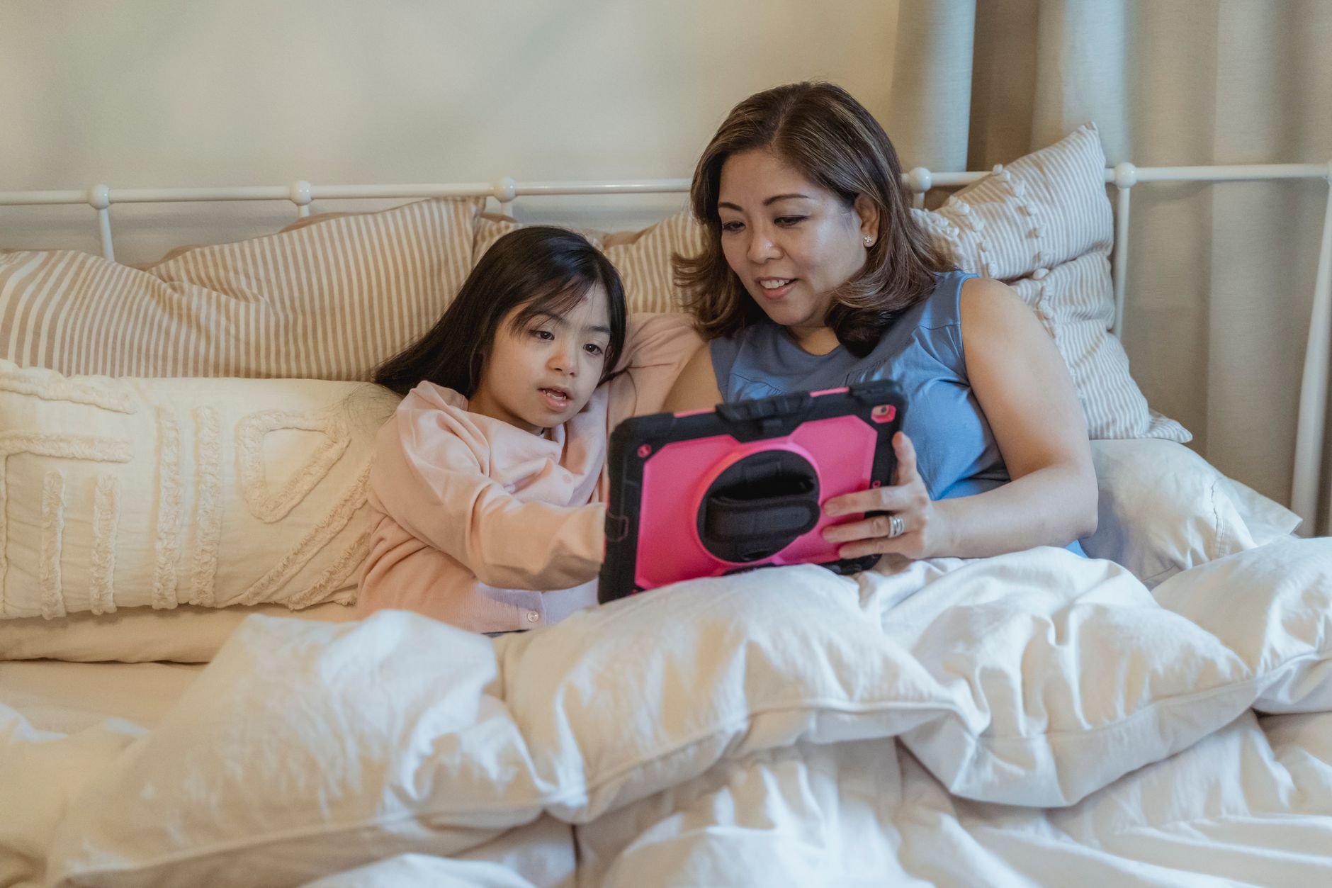 A cozy mother and daughter bonding time with a tablet in bed, showcasing family togetherness